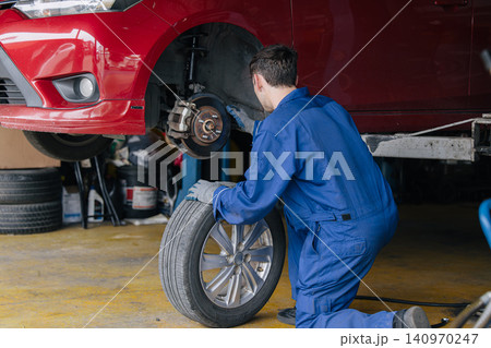 Auto mechanic worker changing car tire in auto workshop garage, Vehicle tyre maintenance service Auto mechanic worker changing car tire in auto workshop garage, Vehicle tyre maintenance service 140970247
