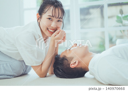 昼寝する彼氏の横で満面の笑顔を見せる彼女の幸せいっぱいなカップルシーン 140970668