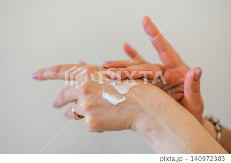 Close-up of elegant female hands with a light manicure applying moisturizing cream - showcasing gentle hand care and beauty treatment 140972383