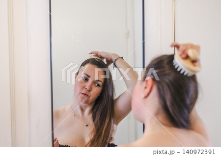 A woman gently combs her hair as part of her daily beauty care routine, promoting healthy, smooth, and well-groomed locks. A woman gently combs her hair as part of her daily beauty care routine, promoting healthy, smooth, and well-groomed locks. 140972391
