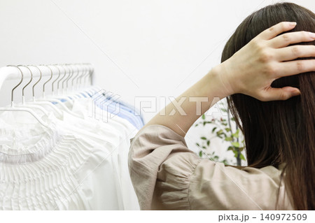 ハンガーラックに並んだ服を見ながら悩む女性の後ろ姿 140972509