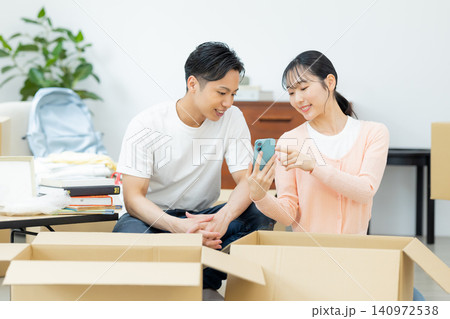 引越し 荷物を片付けながらスマホを見るカップル 引越し 荷物を片付けながらスマホを見るカップル 140972538