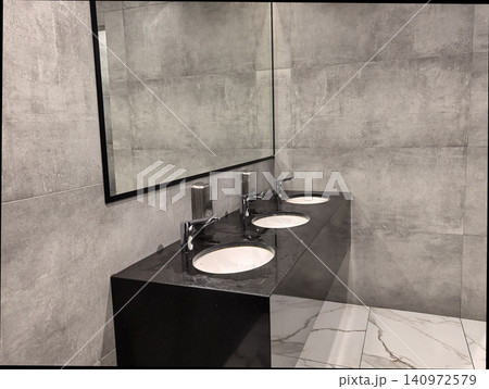 Modern public restroom with three white sinks on black granite countertop Modern public restroom with three white sinks on black granite countertop 140972579