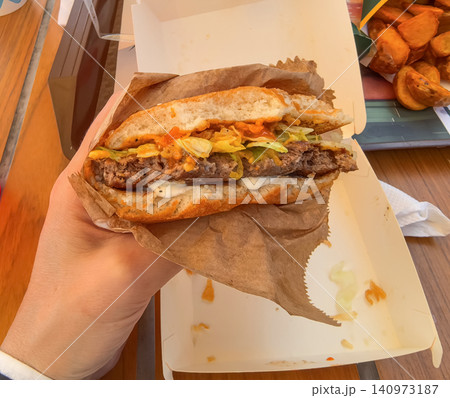 Hand holding a juicy beef burger with lettuce and sauce over takeout box Hand holding a juicy beef burger with lettuce and sauce over takeout box 140973187