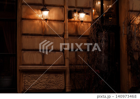 Old building facade with vintage lanterns casting warm light on a dark night Old building facade with vintage lanterns casting warm light on a dark night 140973468