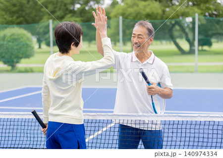テニスでハイタッチをする笑顔のシニア夫婦・ダブルスの勝利 テニスでハイタッチをする笑顔のシニア夫婦・ダブルスの勝利 140974334