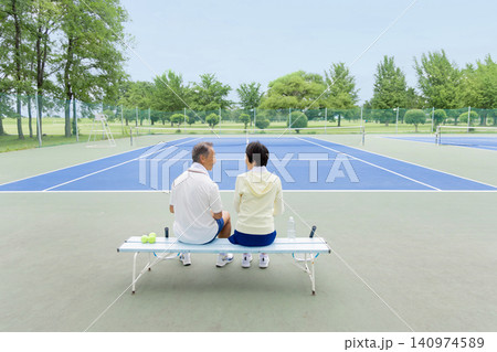 テニスコートのベンチで休憩するシニア夫婦の後ろ姿 テニスコートのベンチで休憩するシニア夫婦の後ろ姿 140974589