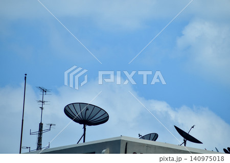 Satellite dishes with tv antenna on top of the old gray building against the sky. Satellite dish with sky on the roof. The satellite dishes, and TV antennas on the roof building in urban. Satellite dishes with tv antenna on top of the old gray building against the sky. Satellite dish with sky on the roof. The satellite dishes, and TV antennas on the roof building in urban. 140975018