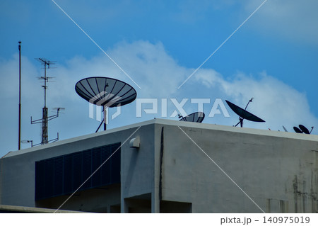 Satellite dishes with tv antenna on top of the old gray building against the sky. Satellite dish with sky on the roof. The satellite dishes, and TV antennas on the roof building in urban. Satellite dishes with tv antenna on top of the old gray building against the sky. Satellite dish with sky on the roof. The satellite dishes, and TV antennas on the roof building in urban. 140975019