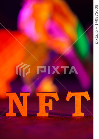 Orange NFT letters standing against vibrant multicolor bokeh lights for blockchain concept 140975608