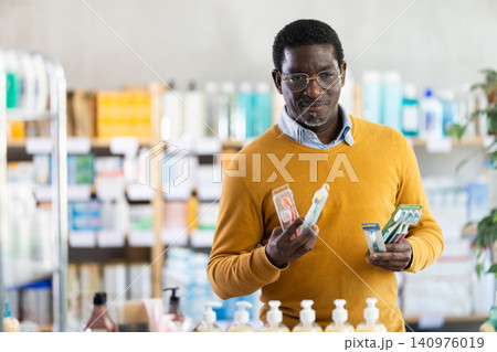 Male shopper in glasses attentively chooses toothbrush in supermarket Male shopper in glasses attentively chooses toothbrush in supermarket 140976019