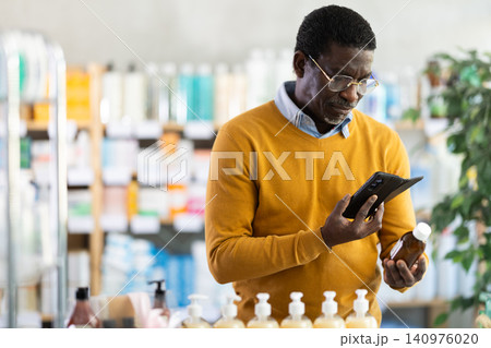 African man in pharmacy scans QR code on expectorant syrup. African man in pharmacy scans QR code on expectorant syrup. 140976020