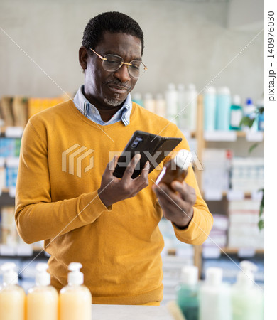 African man in pharmacy scans QR code on expectorant syrup. African man in pharmacy scans QR code on expectorant syrup. 140976030