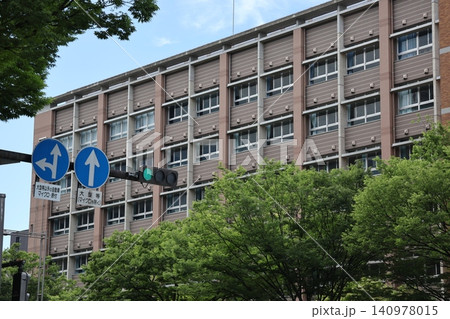 青空と青信号と標識と緑の葉の街路樹と学校の建物のある街並みの風景 140978015