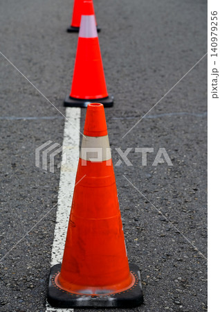 Close-up of the traffic cone on the road. Bright orange traffic cones standing in a row on asphalt. Transportation tool, equipment. Road works. Cityscape. 140979256