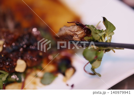 Chopstick-Held Meat with Microgreens on Plate Chopstick-Held Meat with Microgreens on Plate 140979941