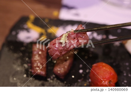 Close-up of Tongs Holding Raw Beef with Garlic Over Slate Plate Close-up of Tongs Holding Raw Beef with Garlic Over Slate Plate 140980069