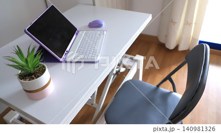 Modern workspace featuring a purple laptop, mouse, and potted plant on a white desk with a gray folding chair in a well-lit room Modern workspace featuring a purple laptop, mouse, and potted plant on a white desk with a gray folding chair in a well-lit room 140981326