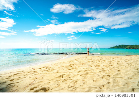 Wide tropical beach with golden sand, turquoise ocean, and blue sky as a solo traveler celebrates freedom by the shoreline. Inspiring summer vacation, tourism, travel destination, and wellness concept Wide tropical beach with golden sand, turquoise ocean, and blue sky as a solo traveler celebrates freedom by the shoreline. Inspiring summer vacation, tourism, travel destination, and wellness concept 140983301