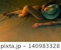 Top view of a woman relaxing on tropical beach as gentle waves wash across sand during golden sunset. Peaceful summer vacation, luxury travel, wellness lifestyle, seaside escape, and coastal serenity. 140983328