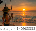 Golden sunset reflecting across the tropical ocean as a woman enjoys beach swing beside gentle waves. Luxury vacation, serene coastal destination, summer travel, relaxation, mindfulness, and wellness. 140983332