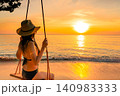 Woman relaxing on a beach swing while watching a golden tropical sunset over the calm ocean. Peaceful summer vacation, luxury travel, wellness lifestyle, seaside serenity, and coastal escape. 140983333