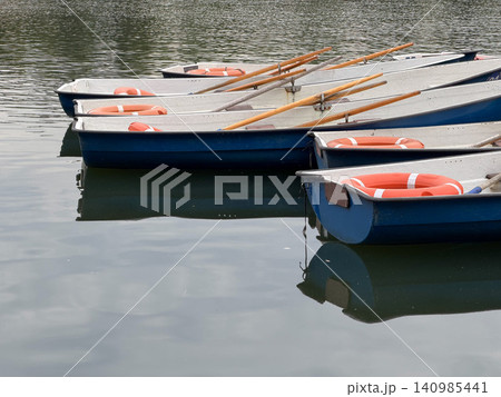 Blue and white rowing boat moored on calm lake with wooden oars. Recreation, leisure, tourism, watersports, summer travel, outdoor lifestyle, vacation marketing Blue and white rowing boat moored on calm lake with wooden oars. Recreation, leisure, tourism, watersports, summer travel, outdoor lifestyle, vacation marketing 140985441