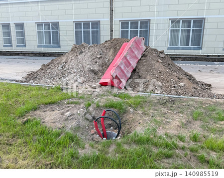 Construction site with soil mound and red debris chute beside institutional building. Urban development, engineering, infrastructure, renovation, municipal improvement, property maintenance Construction site with soil mound and red debris chute beside institutional building. Urban development, engineering, infrastructure, renovation, municipal improvement, property maintenance 140985519
