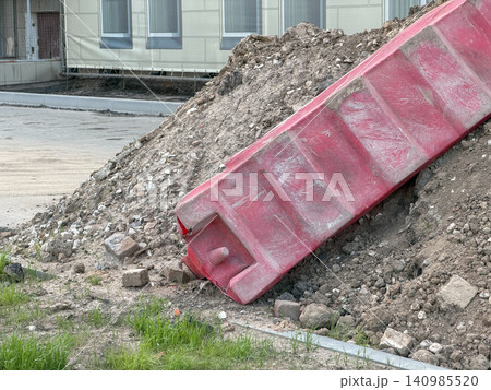 Red construction debris chute resting on soil pile near building during renovation work. Construction, demolition, infrastructure, urban development, engineering, waste management. Red construction debris chute resting on soil pile near building during renovation work. Construction, demolition, infrastructure, urban development, engineering, waste management. 140985520