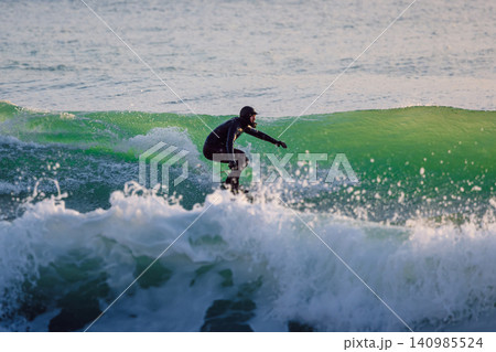 Surfer man riding on perfect wave in ocean with sunset tones Surfer man riding on perfect wave in ocean with sunset tones 140985524