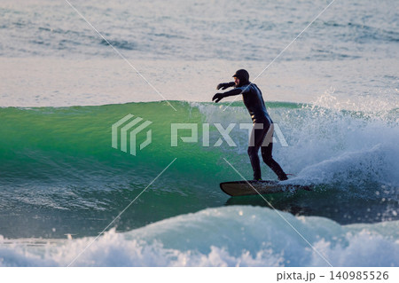 Surfer male rides and pumping on glassy wave in sea with evening sunlight 140985526