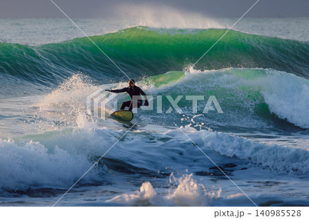 Surfer on wave in cold ocean. Winter surfing with evening sunlight Surfer on wave in cold ocean. Winter surfing with evening sunlight 140985528