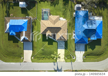 Hurricane Ian damaged house rooftop covered with protective plastic tarp against rain water leaking until replacement of asphalt shingles. Aftermath of natural disaster Hurricane Ian damaged house rooftop covered with protective plastic tarp against rain water leaking until replacement of asphalt shingles. Aftermath of natural disaster 140985634