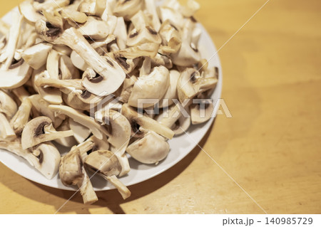Sliced button mushrooms on white plate ready for cooking on wood Sliced button mushrooms on white plate ready for cooking on wood 140985729