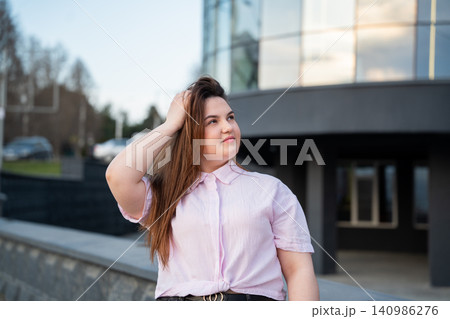 Confident young professional woman in casual attire outside modern glass office building. Corporate lifestyle urban workplace and career success 140986276