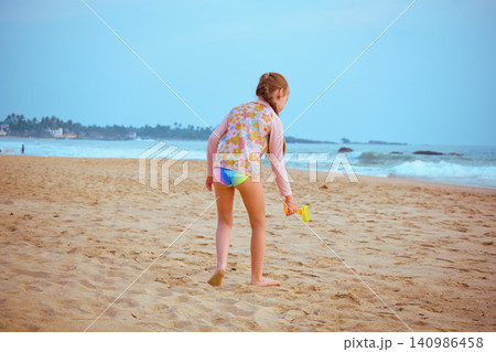 Little girl playing with yellow shovel on tropical beach Hikkaduwa Sri Lanka 140986458