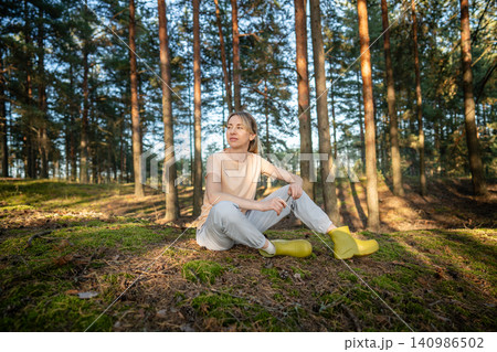 Smiling tranquil woman relaxing in autumn forest alone, sitting on meadow under warm sunlight. Smiling tranquil woman relaxing in autumn forest alone, sitting on meadow under warm sunlight. 140986502