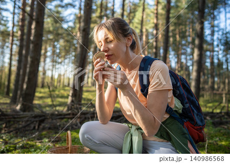Woman forager holding boletus mushroom and smelling scent, picking porcini mushroom in autumn forest Woman forager holding boletus mushroom and smelling scent, picking porcini mushroom in autumn forest 140986568