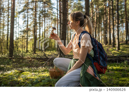 Woman hiker backpacker collecting mushrooms in woods, kneeling on ground holding Boletus edulis find Woman hiker backpacker collecting mushrooms in woods, kneeling on ground holding Boletus edulis find 140986626