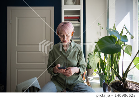 Calm mature woman listening to music in wired headphones using streaming service app on smartphone 140986628