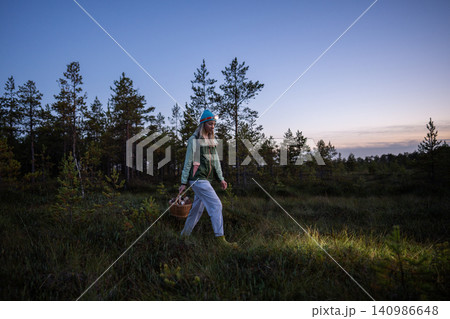 Woman walks in autumn swamp forest with basket mushrooms at dusk, lighting way with headlamp on head Woman walks in autumn swamp forest with basket mushrooms at dusk, lighting way with headlamp on head 140986648
