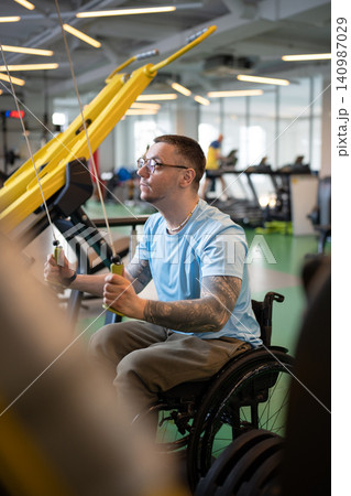 Concentrated disabled man in wheelchair working on spinal injury rehabilitation in sports center. 140987029