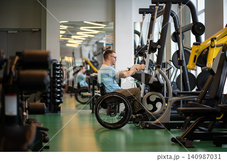 Disabled man in wheelchair working on increasing upper body strength levels with ergometer machine. 140987031