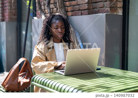 Thoughtful african american woman student working on laptop outdoors in city cafe on sunny day. 140987032