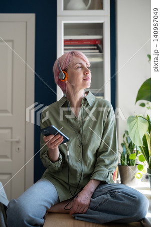Relaxed mature woman using online music on-demand web streaming media platform on smartphone. Relaxed mature woman using online music on-demand web streaming media platform on smartphone. 140987049