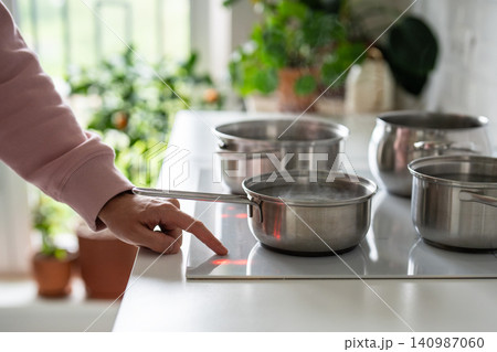 Planned hot water outage and overusing household electricity system, person boiling water on stove. 140987060
