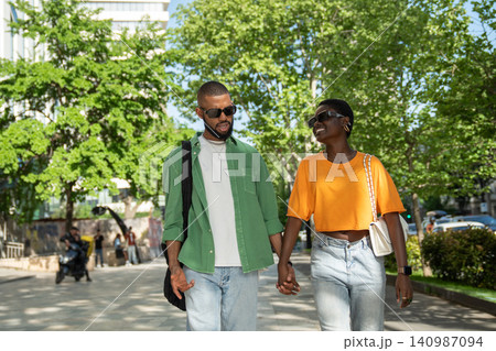 Joyful african american loving couple walking hold hands in city street guy makes girlfriend laugh. Joyful african american loving couple walking hold hands in city street guy makes girlfriend laugh. 140987094