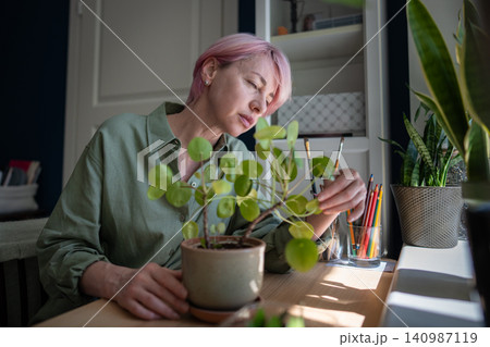 Focused mature woman plant lover inspecting potted Pilea peperomioides plant leaves condition 140987119