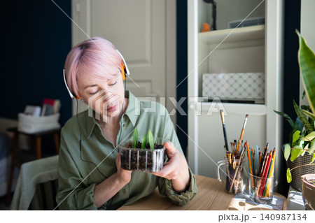 Relaxed mature woman plant lover enjoying indoor garden hobby, holding box with growing seedlings 140987134