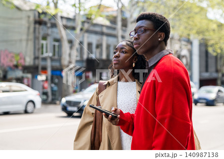 Concentrated african american man and woman tourists wait for taxi while standing on street. Concentrated african american man and woman tourists wait for taxi while standing on street. 140987138